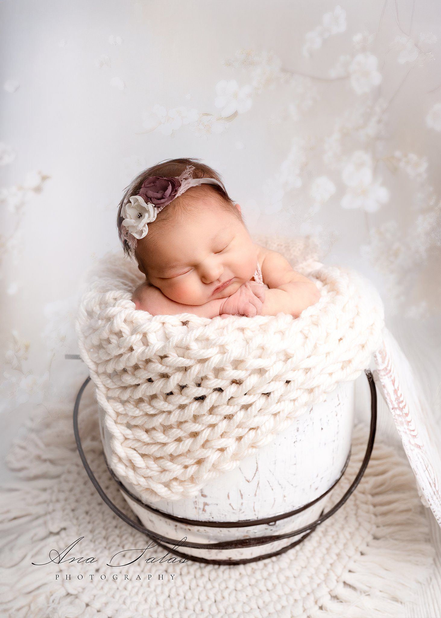 A newborn baby girl sleeps in a bucket on a white blanket with flowers in her hair after visiting one village family chiropractor