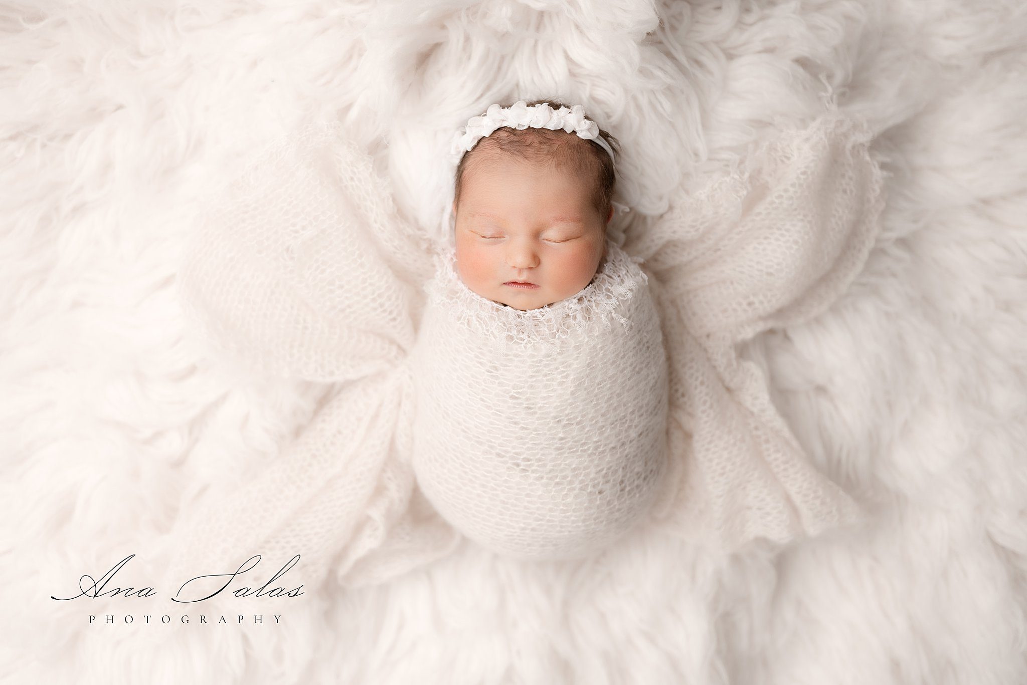 A newborn baby sleeps in a white swaddle in a studio before visiting one village family chiropractor