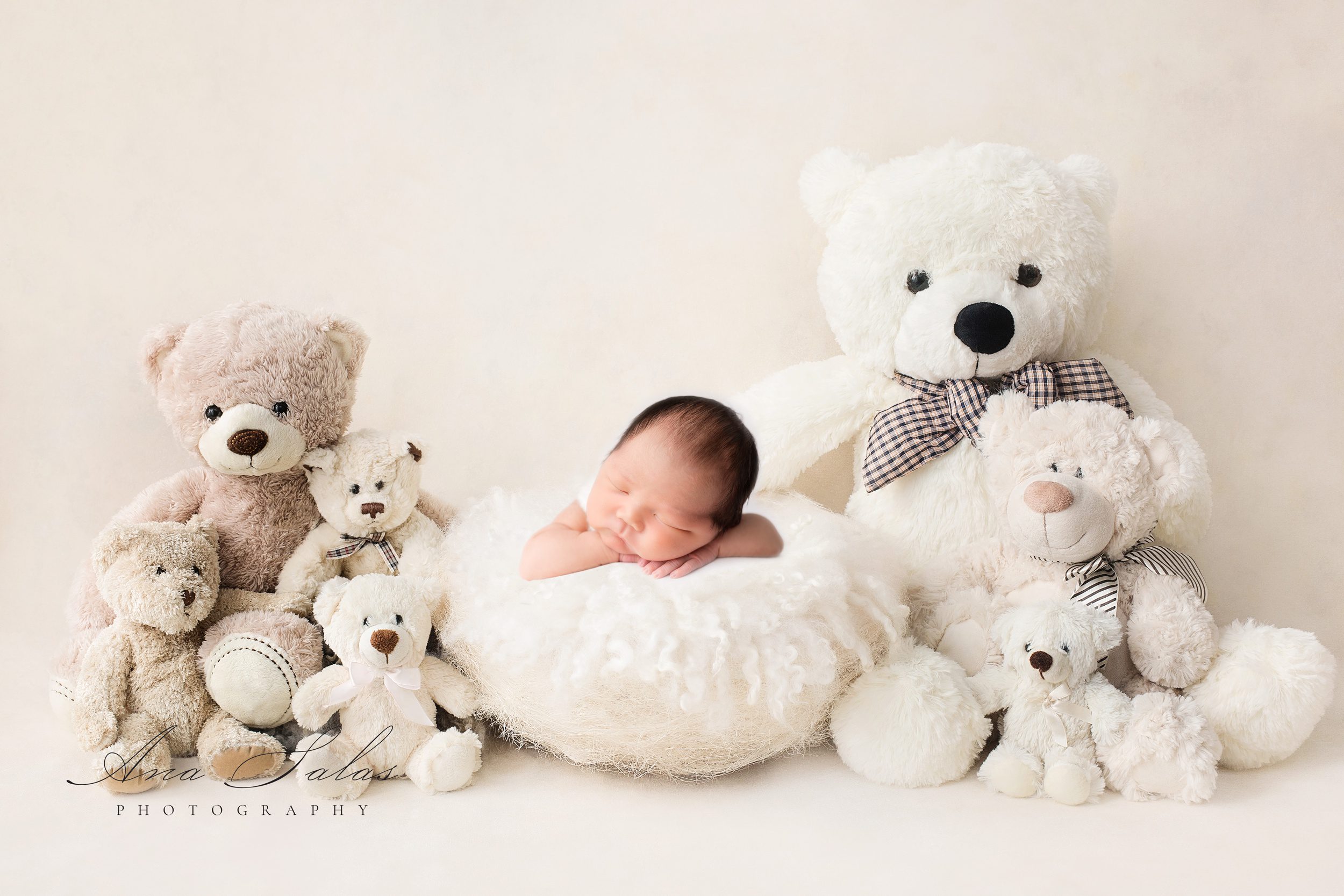 A newborn baby sleeps on a white pillow surrounded by stuffed bears before some baby classes in edmonton