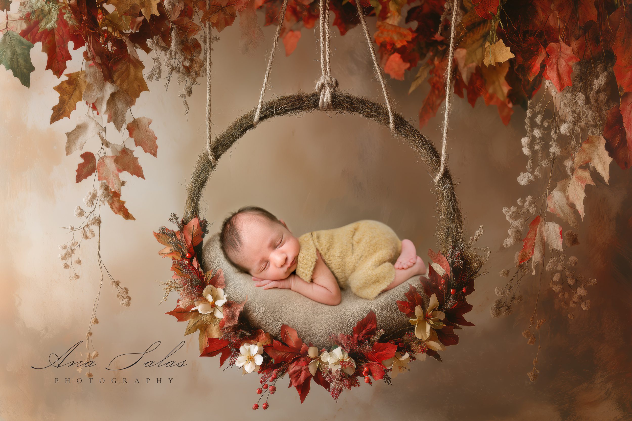 A newborn baby sleeps on a swing surrounded by fall foliage in a studio thanks to baby sleep consultants in edmonton