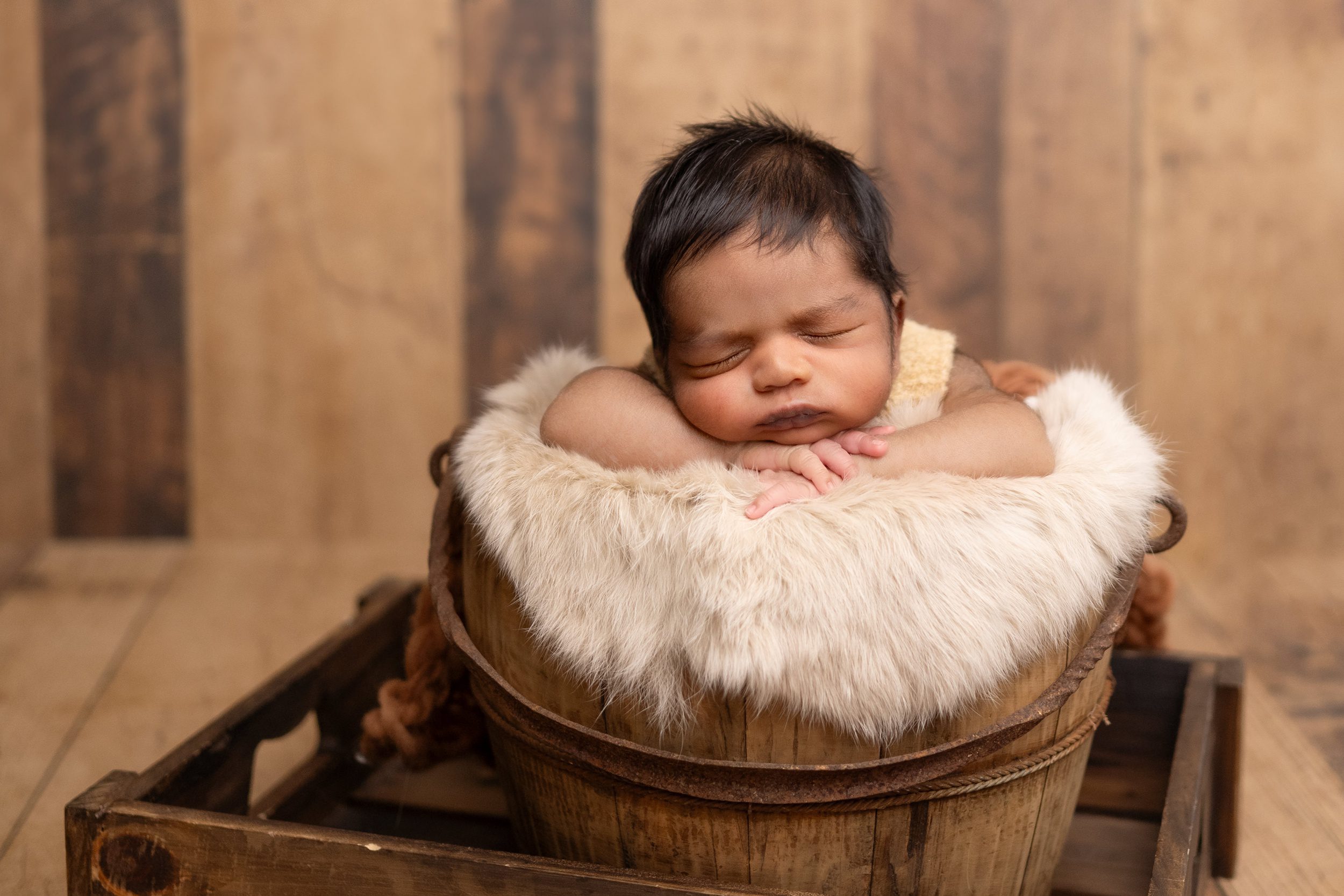 A newborn baby sleeps on a fur blanket in a wooden bucket after meeting baby sleep consultants in edmonton